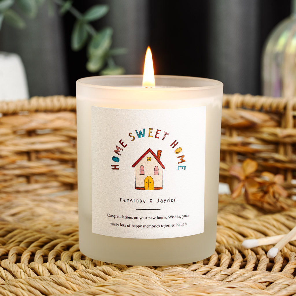 Personalised new home candle with coloured lettering arching over a small red-doored house