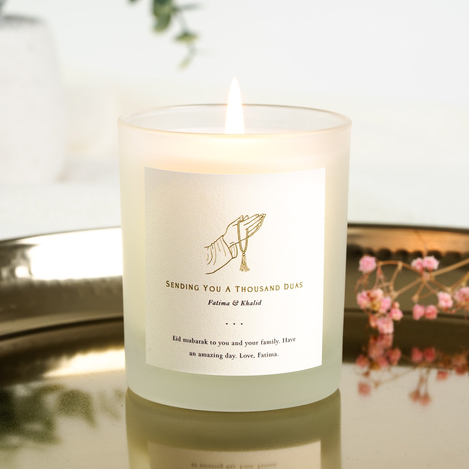 Gold line hand holding a tasselled string of prayer beads on a personalised Eid candle