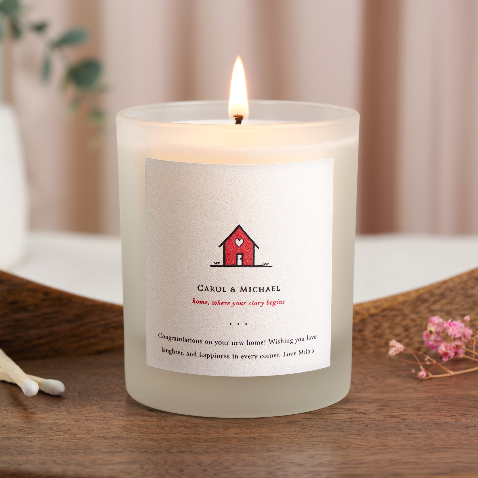 Small red house with a heart cut into its front on a personalised new home candle label