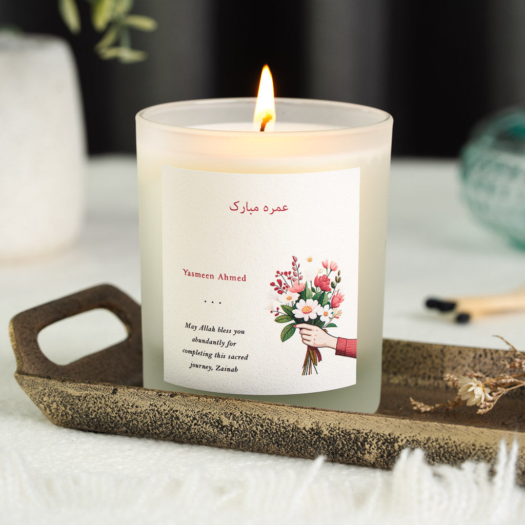 Red Arabic greeting and name beside an illustrated bouquet on a personalised Umrah candle