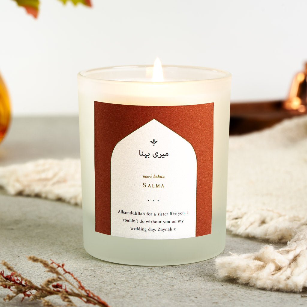 Personalised bridesmaid candle with an Urdu Meri Behna heading inside a white arch on terracotta