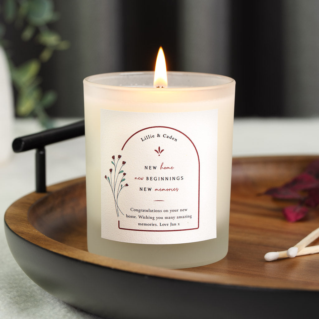 Personalised new home candle with the names inside an arched border beside a line flower