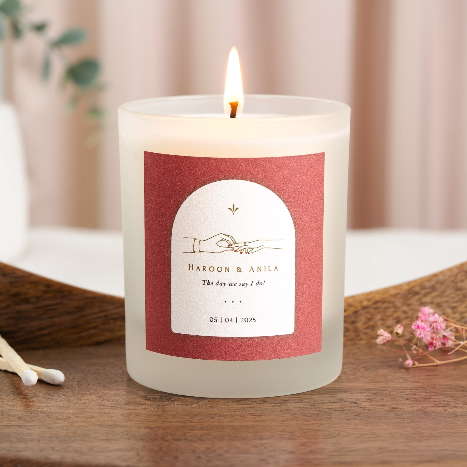 Coral label with a white arch and a line drawing of a ring being placed on a hand, personalised candle