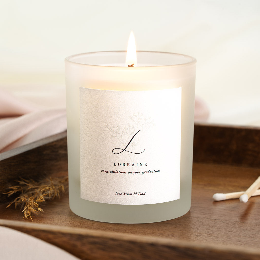 Large script initial above a faint sketched flower sprig on a personalised graduation candle