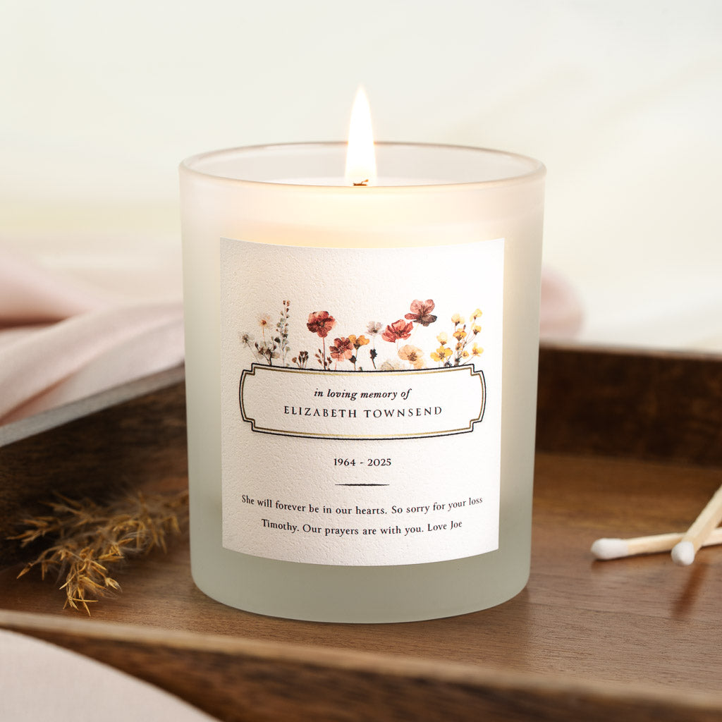 Personalised memorial candle with a row of pressed wildflowers above a bordered nameplate