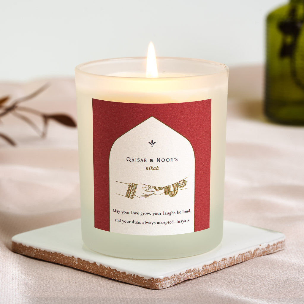 Two hennaed hands touching inside a white arch on a deep red personalised nikah candle