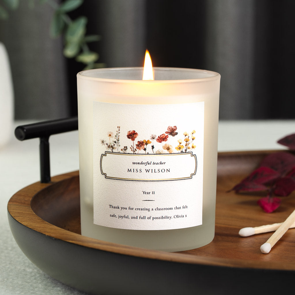 Personalised teacher candle with a pressed wildflower spray above a gold-toned nameplate