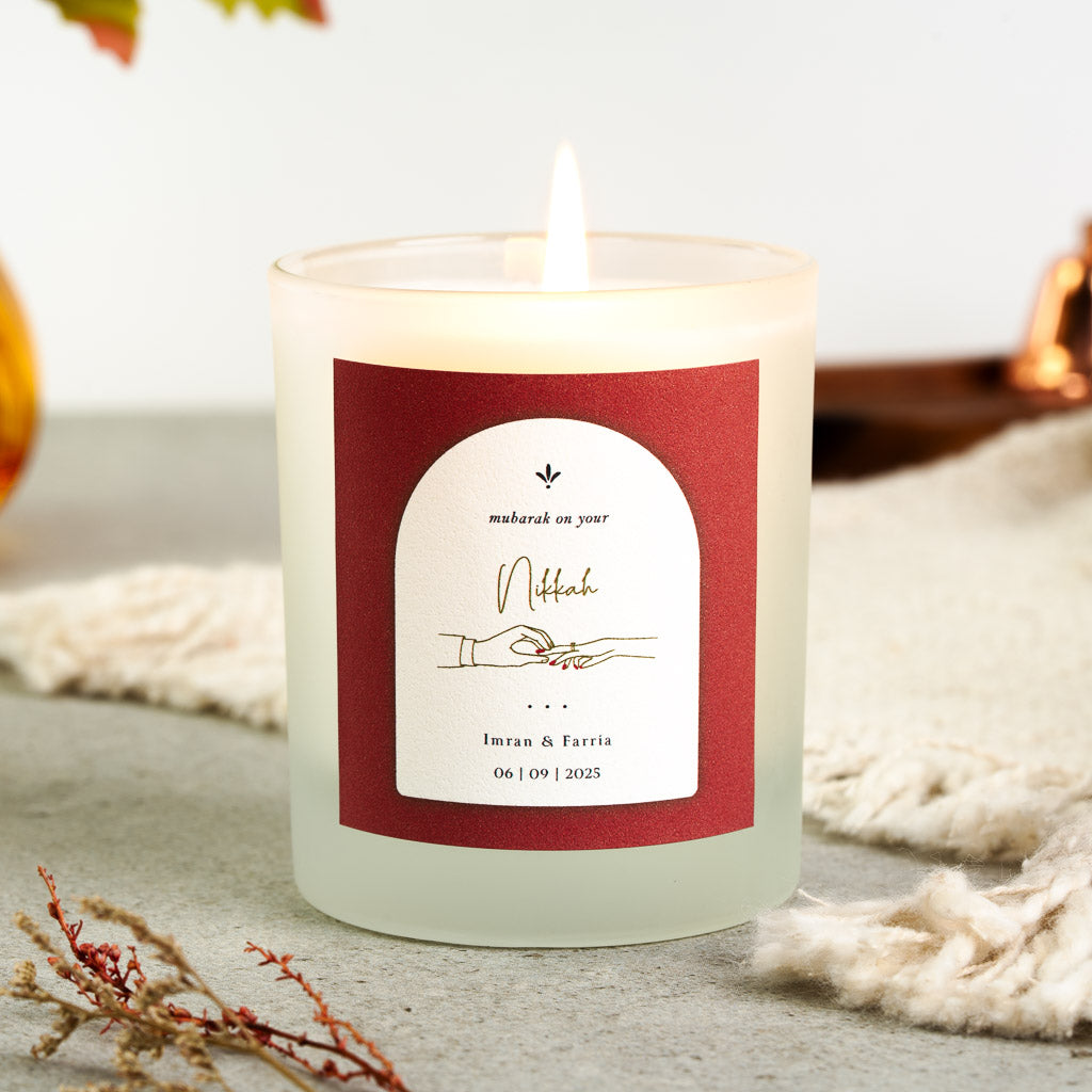 Personalised nikah candle with two hands exchanging rings inside a white arch on rust red