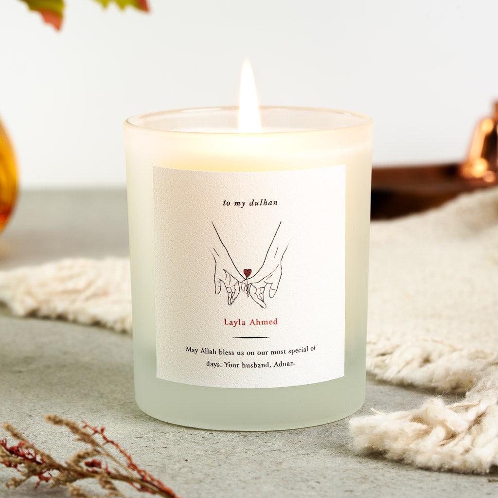 Two hands reaching together with a small red heart on a personalised Islamic wedding candle