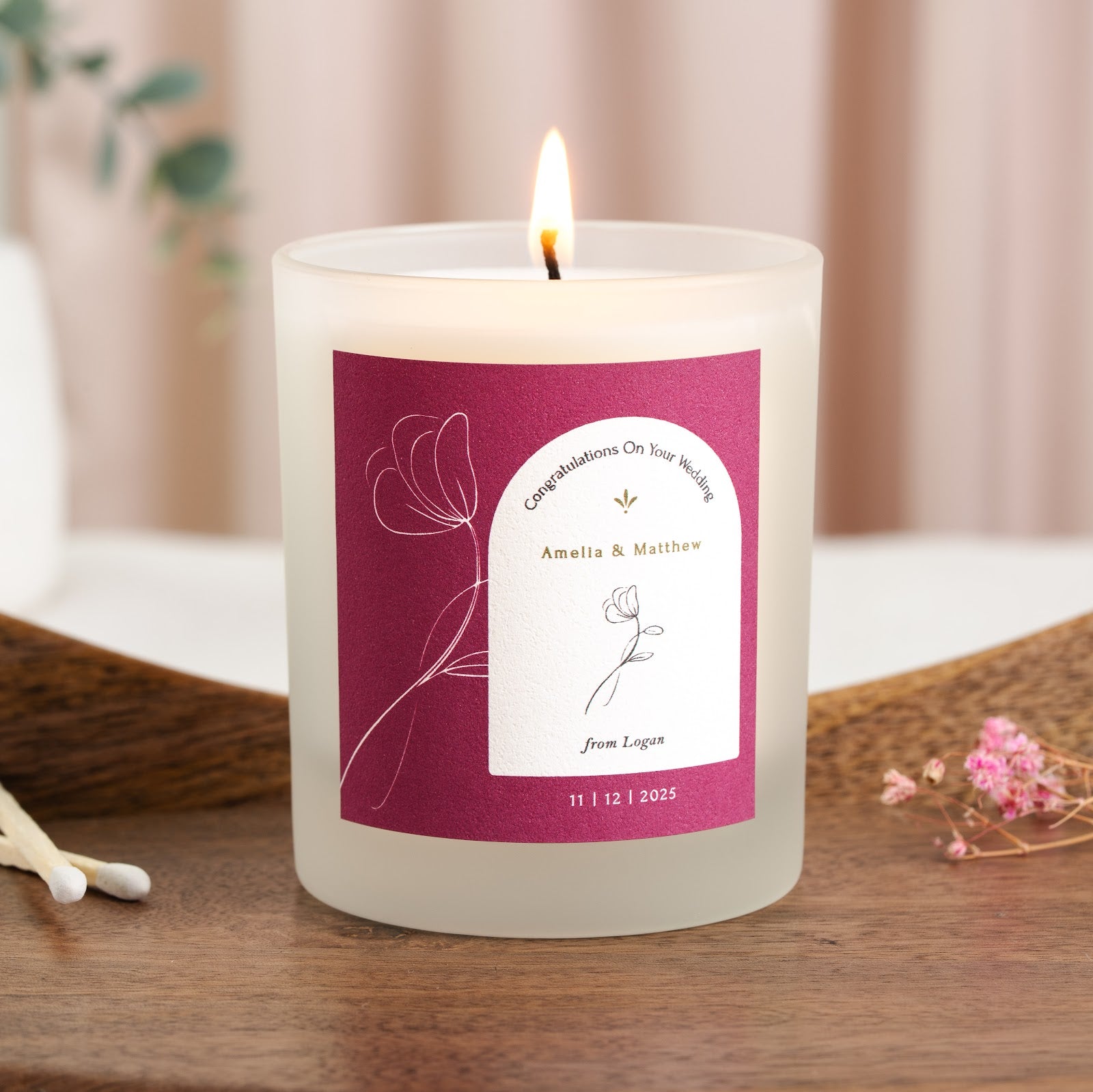 Personalised wedding candle with a magenta label, white floral line art and gold names in an arch