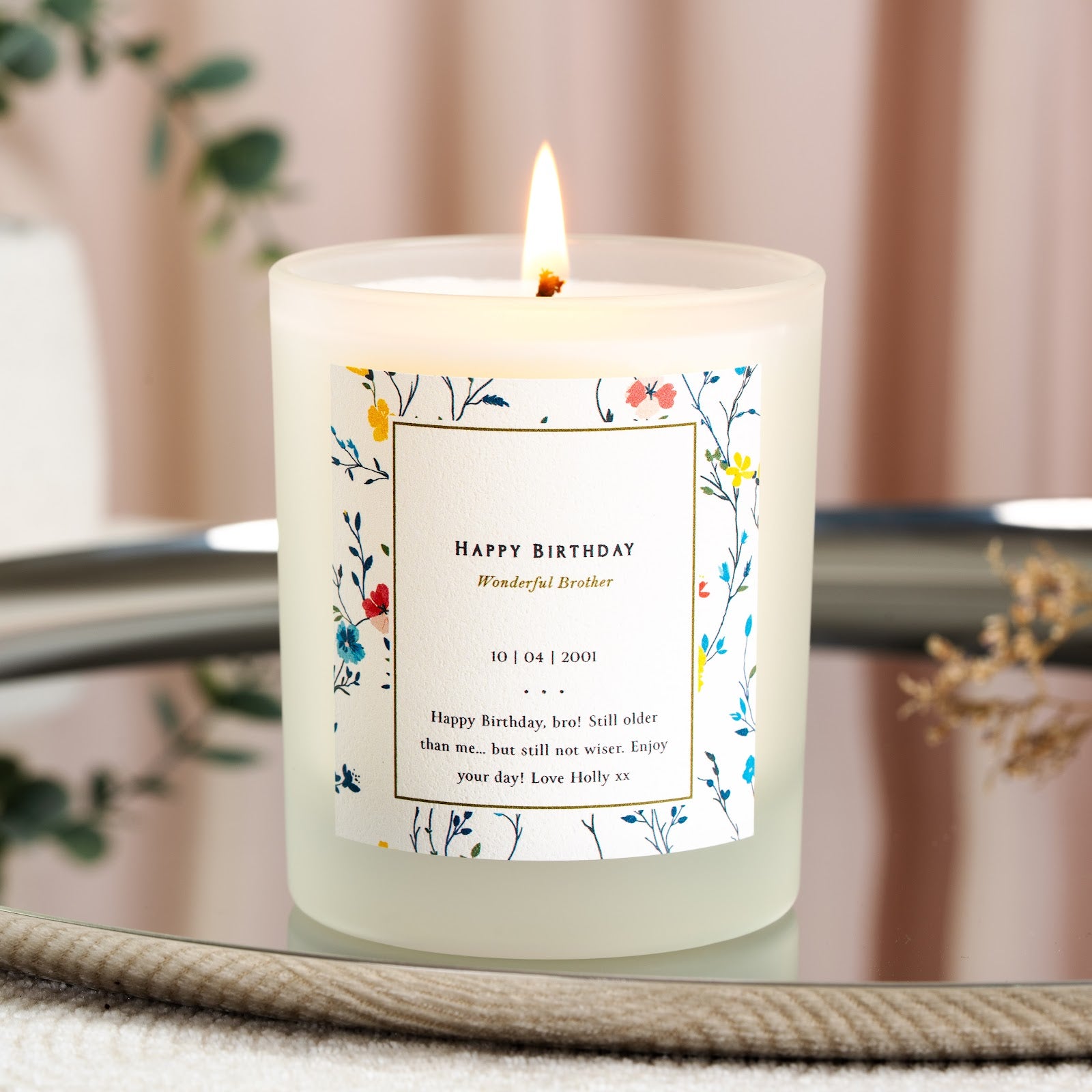 Gold-toned script inside a floral bordered box on a personalised birthday candle label