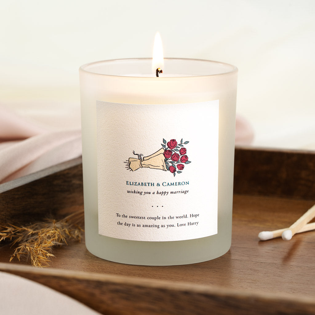 Hand holding a bouquet of red roses on a personalised wedding candle label for couples