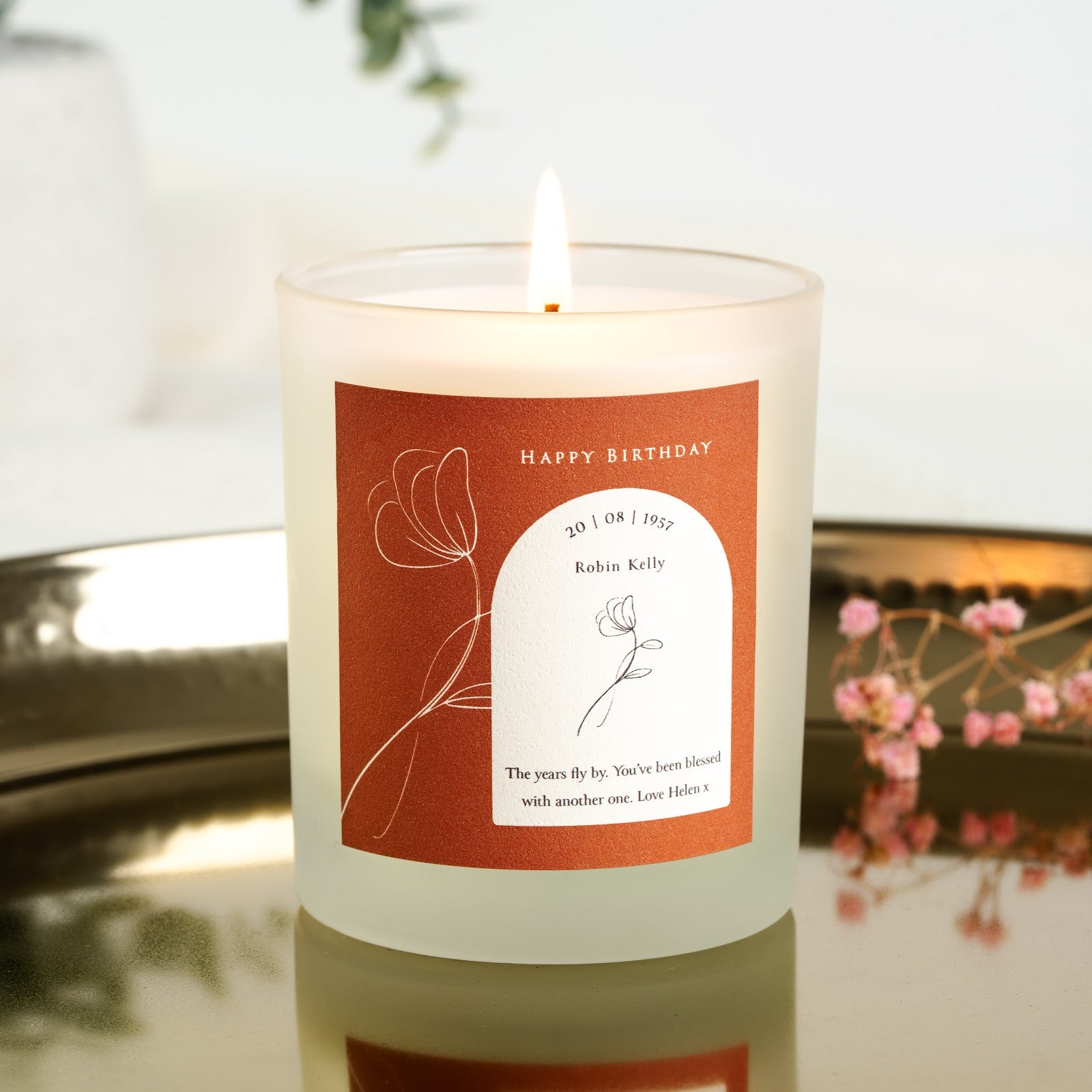 Personalised birthday candle with an outline flower on terracotta beside a white arch