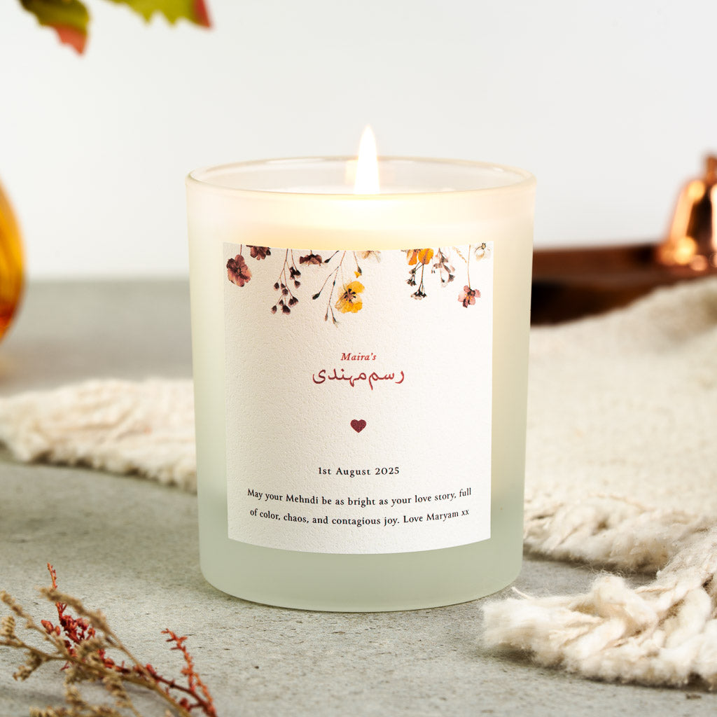 Warm-toned pressed flowers above a red Urdu Rasm-e-Mehndi heading on a personalised candle