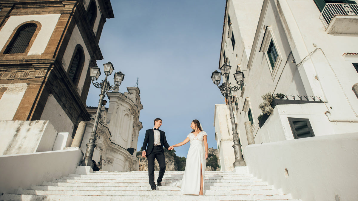 Couple holding hands on a staircase in an urban setting with buildings and clear sky.