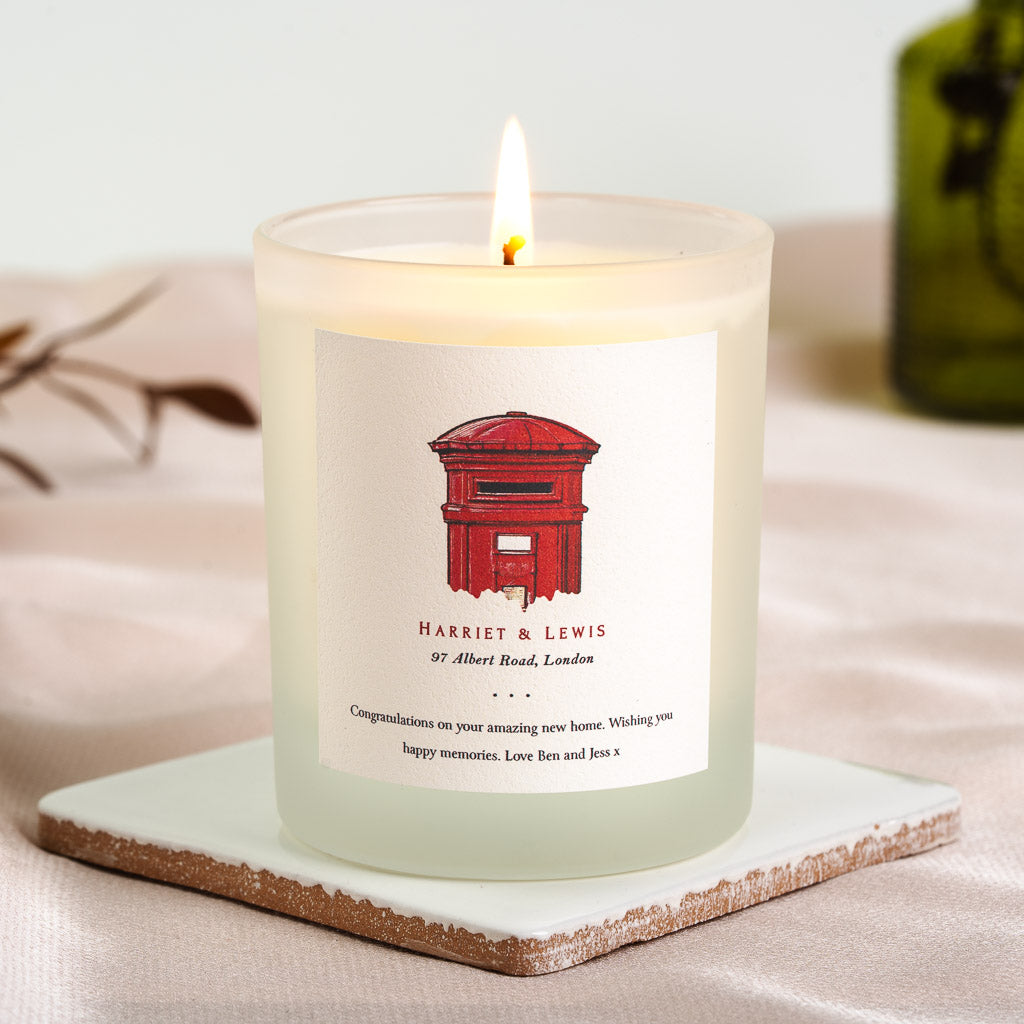 Illustrated post box above the names in deep red serif on a personalised new home candle
