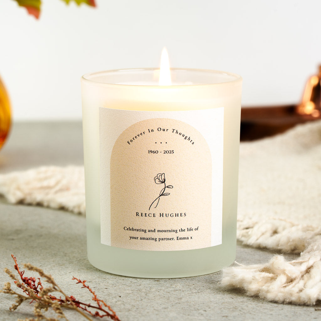 Personalised memorial candle with a line-drawn flower and dates inside a tinted arch above the name