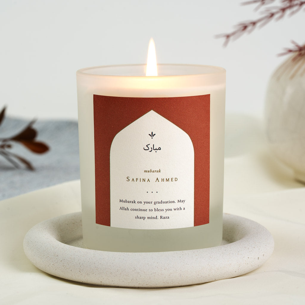 Rust backdrop behind a soft white arch on a personalised Islamic graduation candle