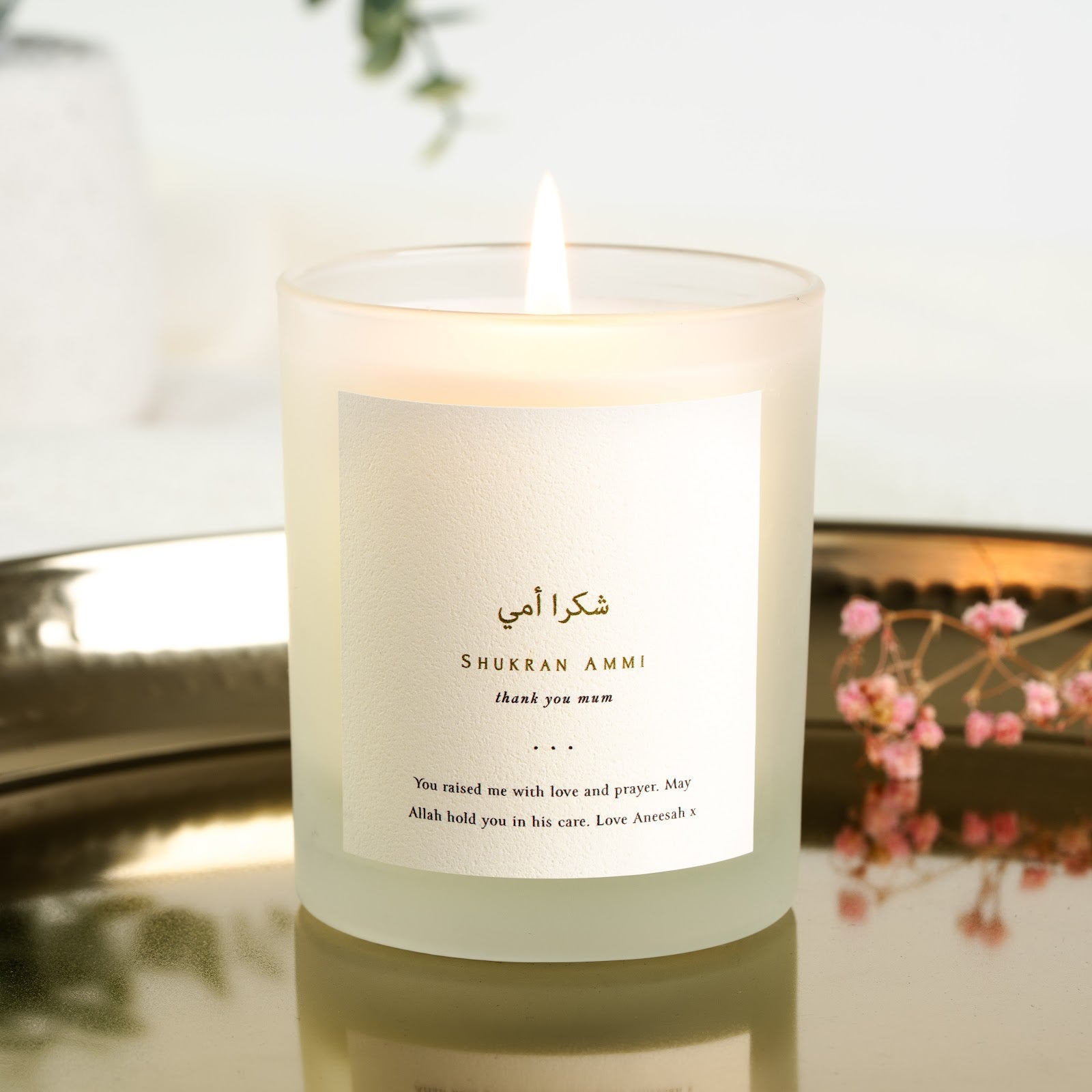 Gold-toned Arabic script above its transliteration on a personalised Mother's Day candle