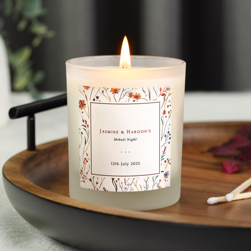Personalised mehndi candle with a square gold panel within scattered pressed wildflowers