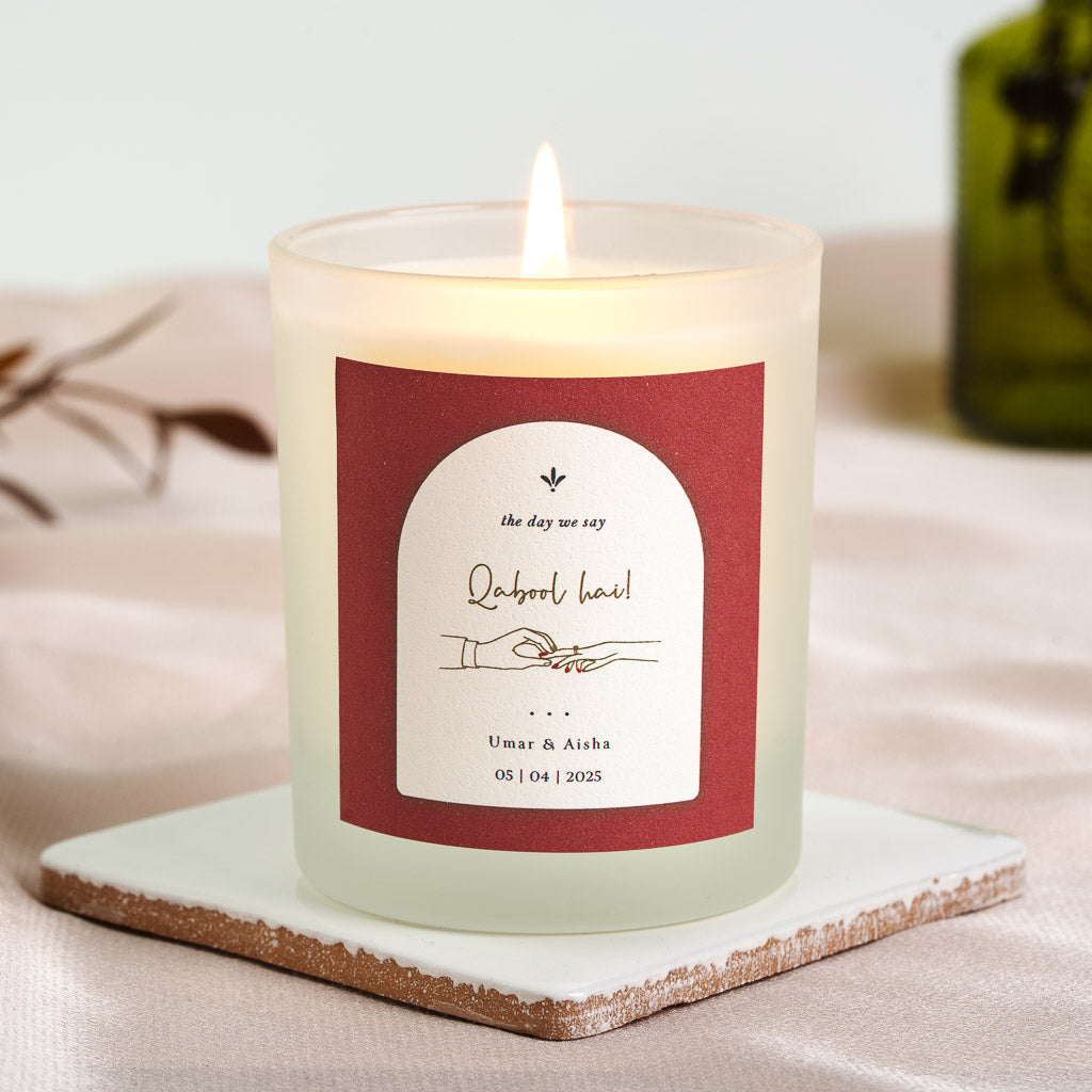 Hand and wrist exchanging a ring inside a white arch on a deep red personalised nikah candle
