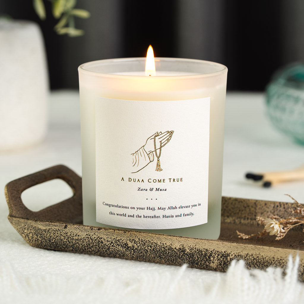 Gold line hand and prayer beads above a duaa line on a personalised Hajj candle label