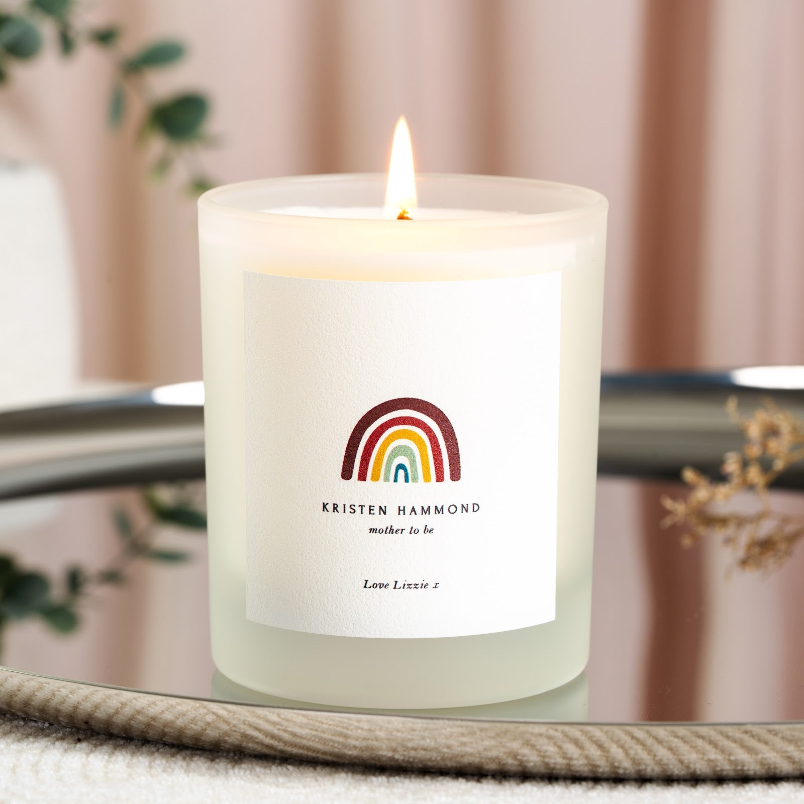Warm rainbow arcs above the name on a personalised mother to be candle label