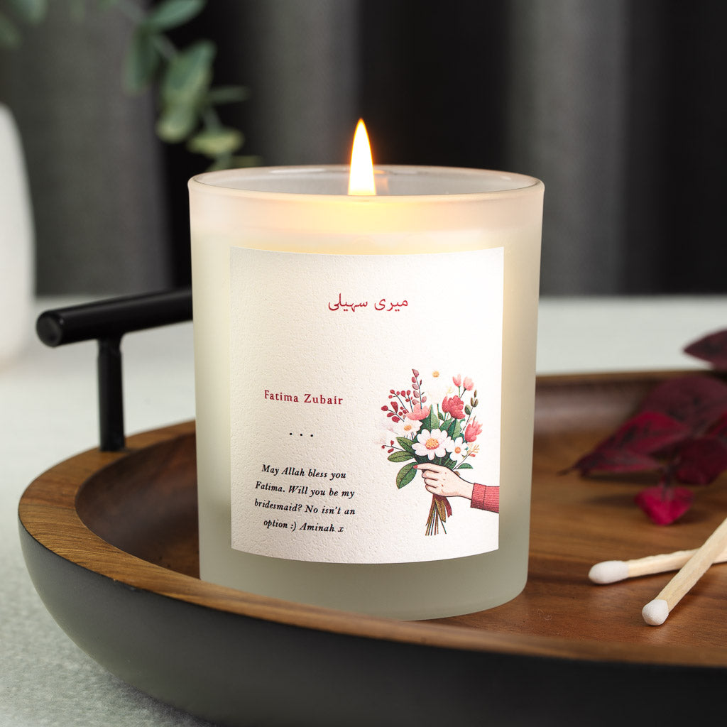 Personalised bridesmaid candle with a hand holding pink and white blooms beneath red Urdu script