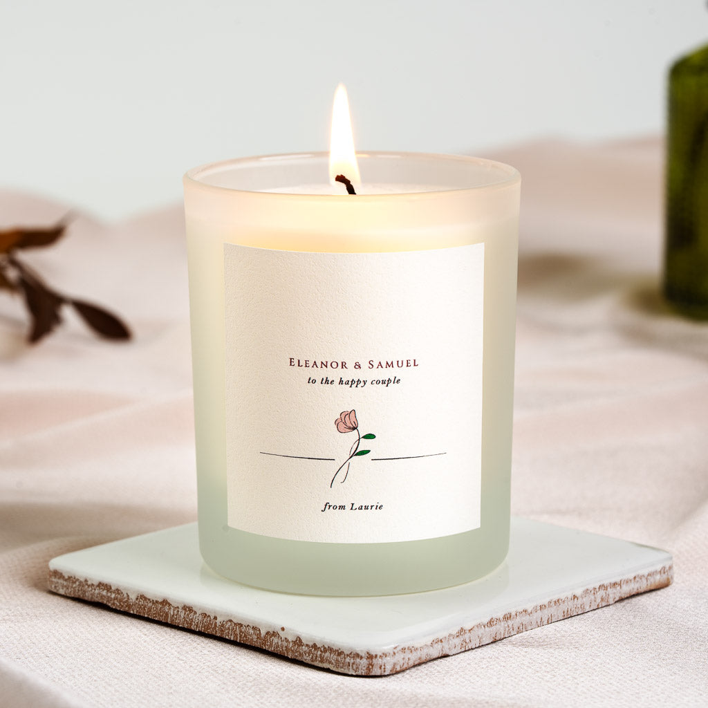 Line-drawn flower resting on a rule beneath to the happy couple on a personalised candle