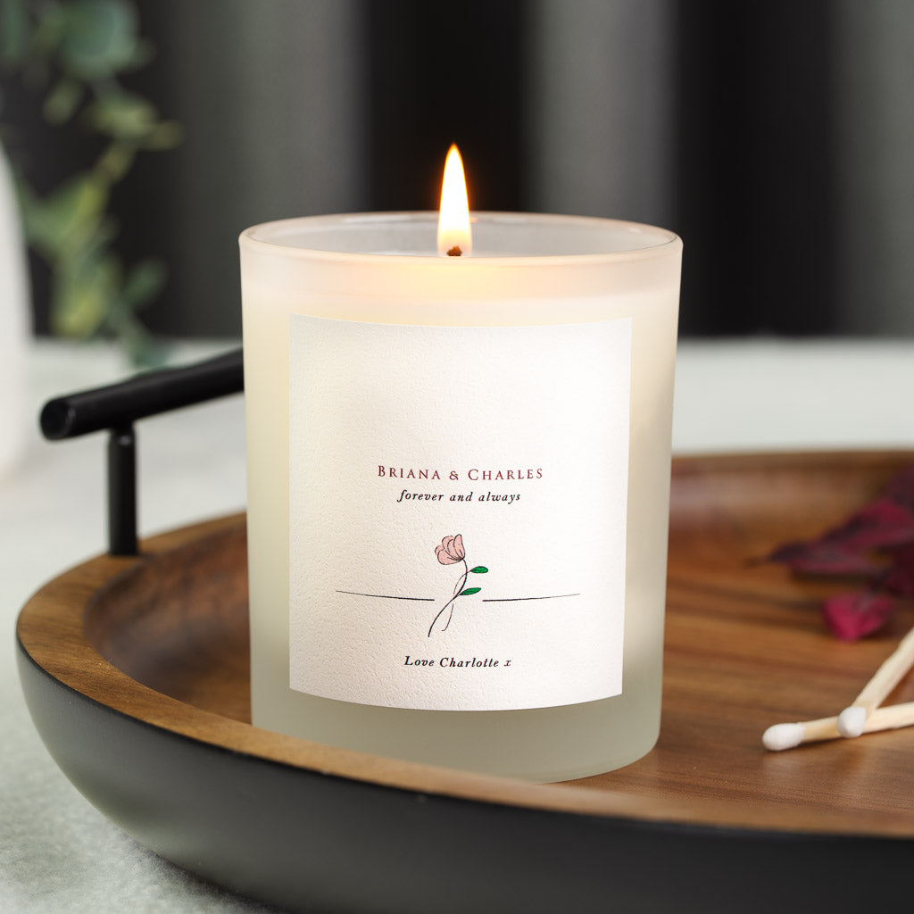Rose sketch beneath the couple's names in deep red serif on a personalised anniversary candle
