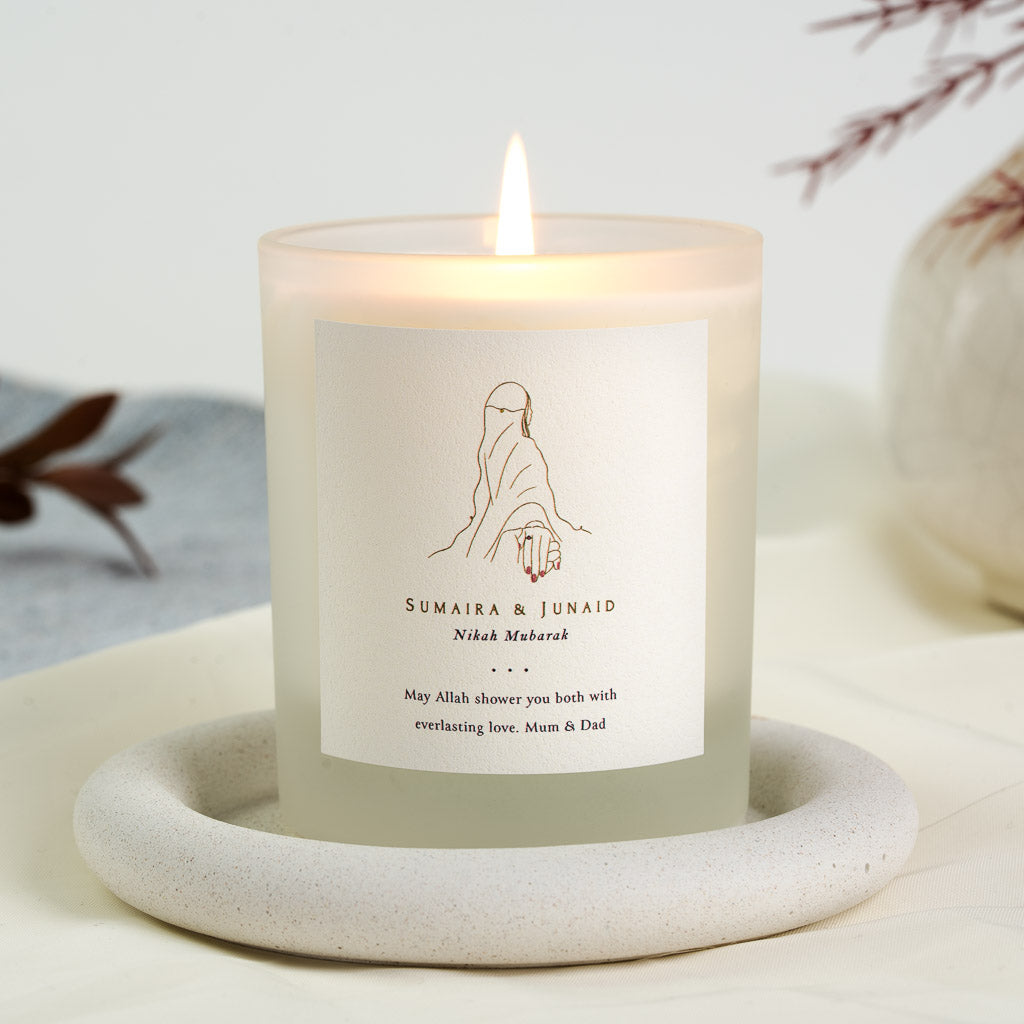 Gold line figure in a hijab with an outstretched hand on a personalised nikah candle