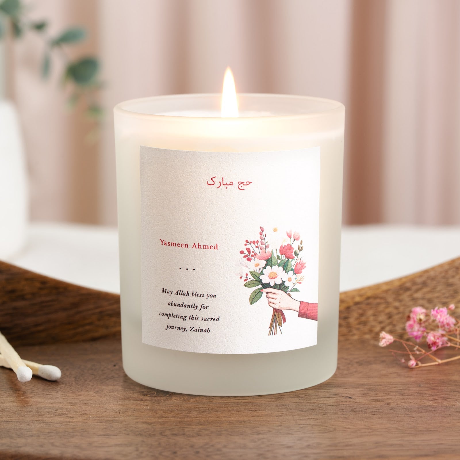Red Arabic greeting and name beside an illustrated bouquet on a personalised Hajj candle
