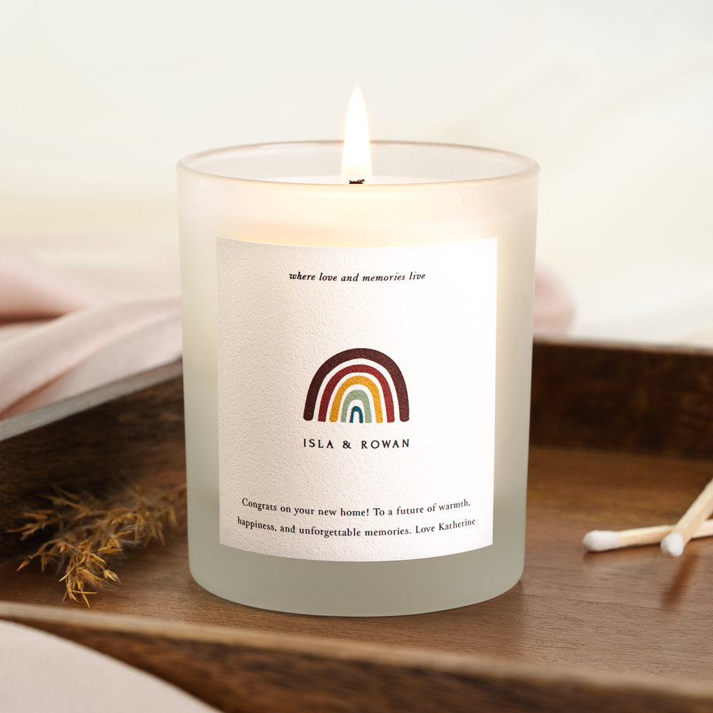 Personalised housewarming candle with a rainbow beneath small italic lettering