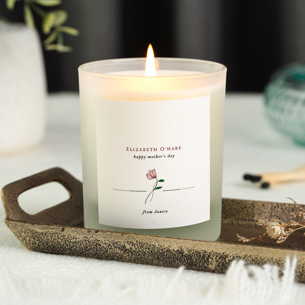 Warm red serif inside an arch with floral sprigs in the corners on a personalised candle