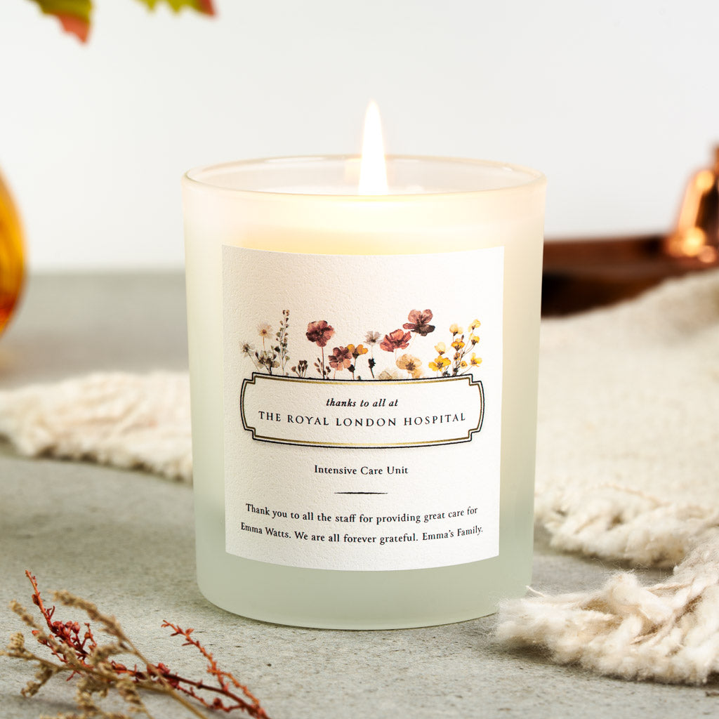 Personalised thank you candle with a row of pressed wildflowers above a bordered nameplate